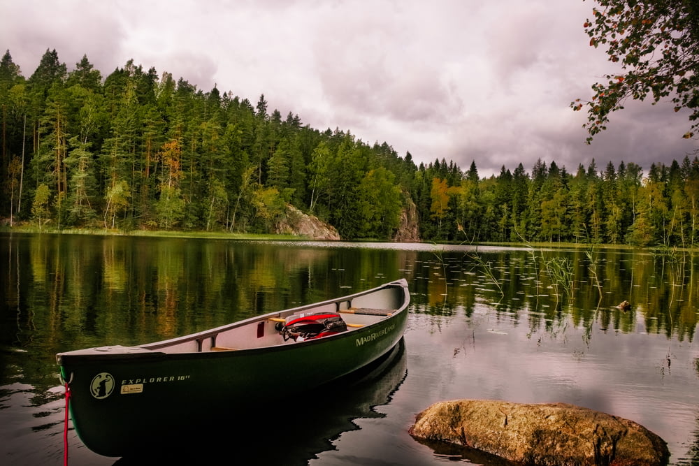 canoa roja y blanca en el lago cerca de los árboles verdes bajo las nubes blancas durante el día