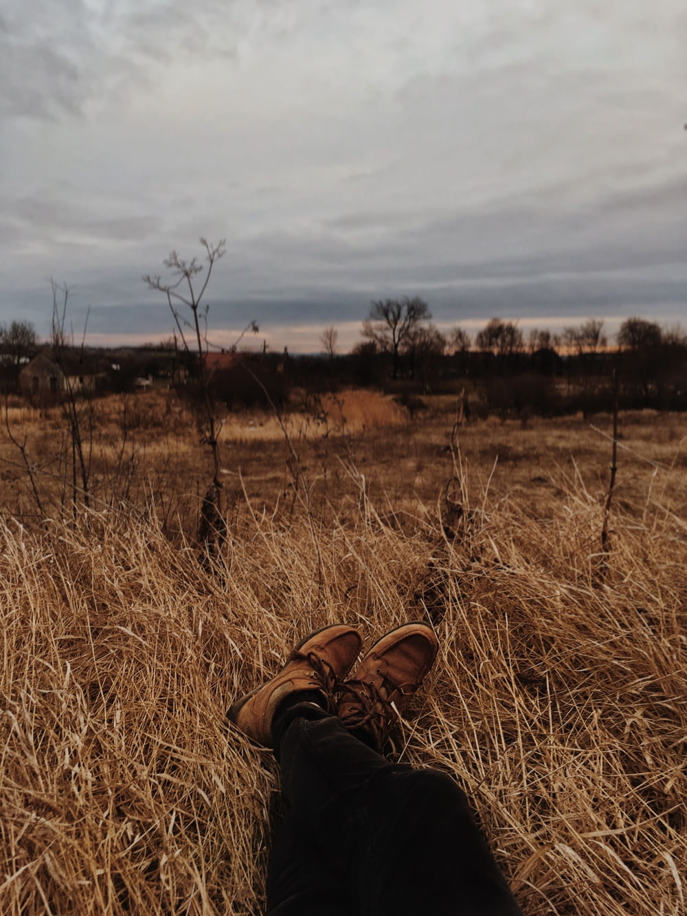 person in brown leather boots sitting on brown grass field during daytime