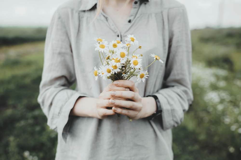 woman in gray long sleeve shirt holding white and yellow flowers