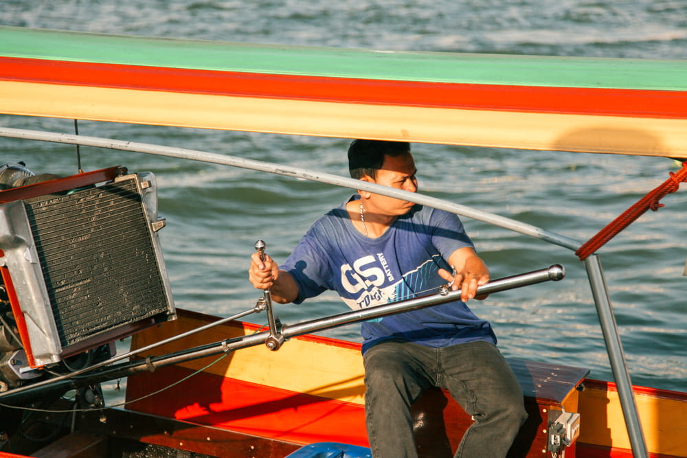 man in blue shirt and blue denim jeans sitting on red and yellow boat during daytime