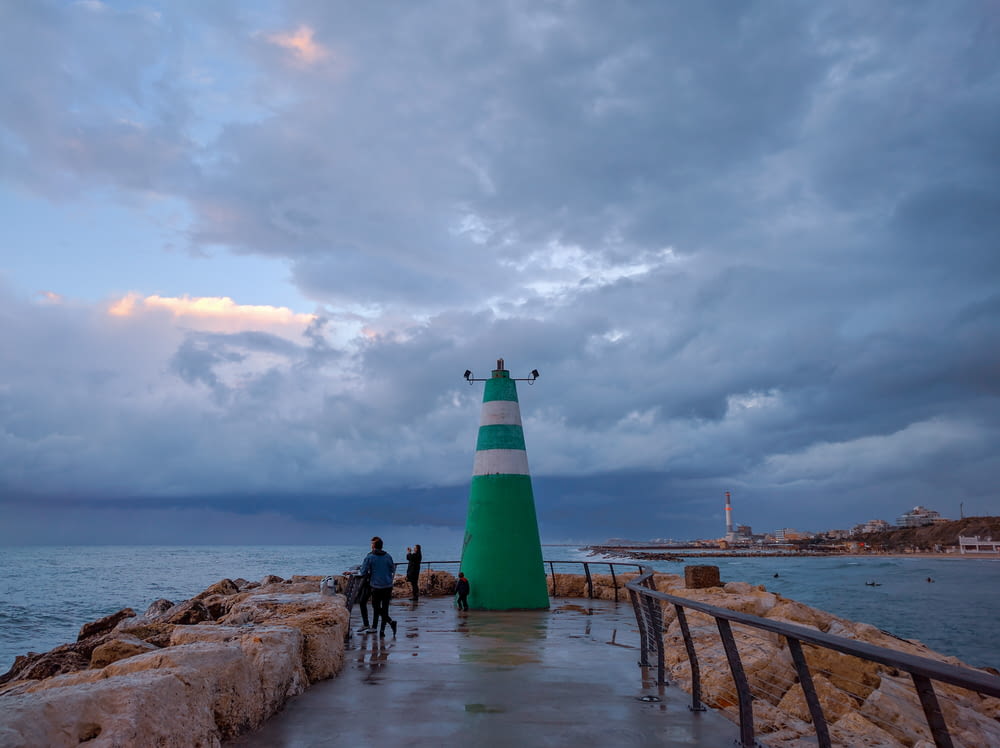 green and white lighthouse near body of water under cloudy sky during daytime