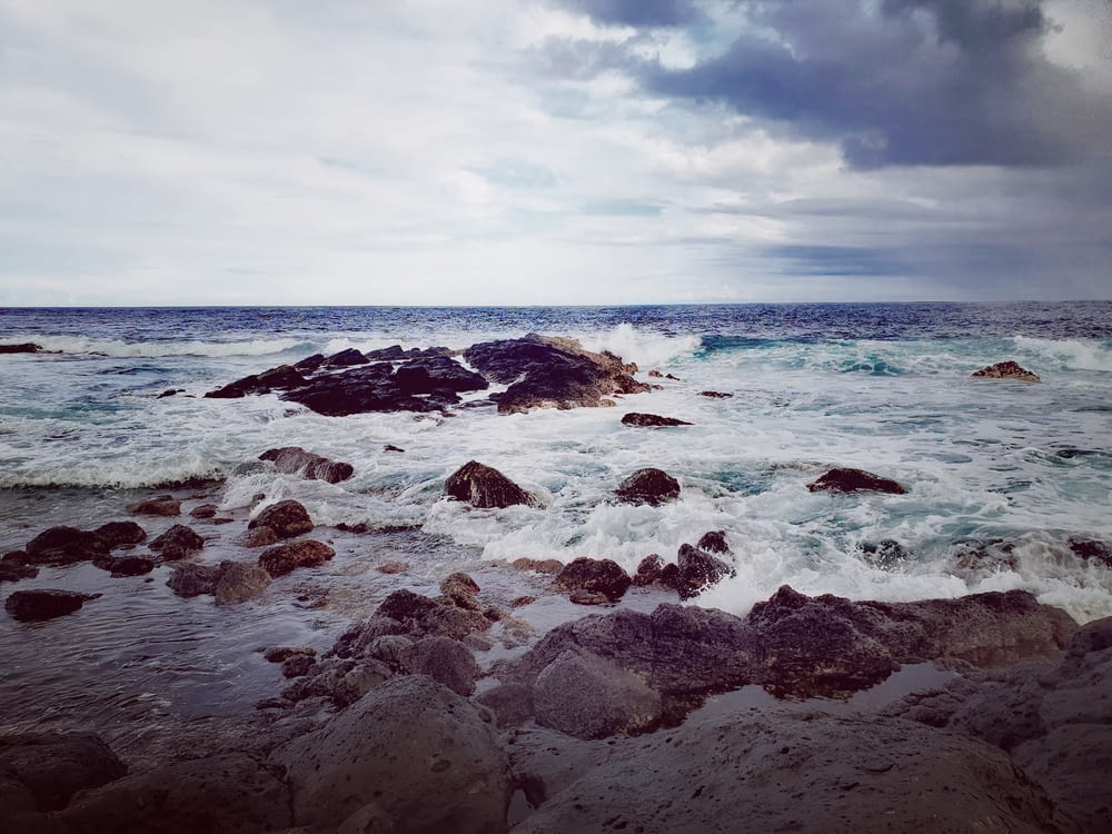 ocean waves crashing on rocky shore under blue and white cloudy sky during daytime