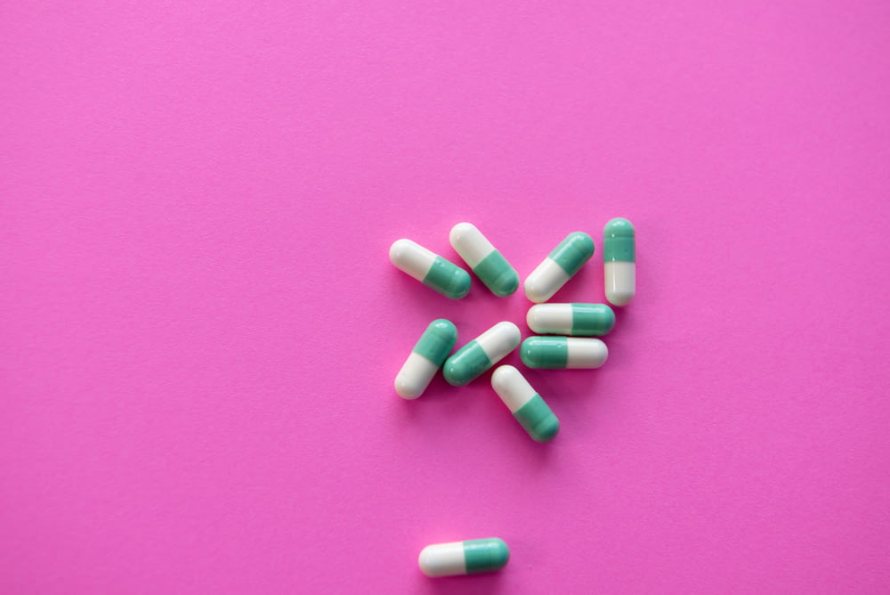 weiße und blaue Medikamentenpille auf rosa Textil