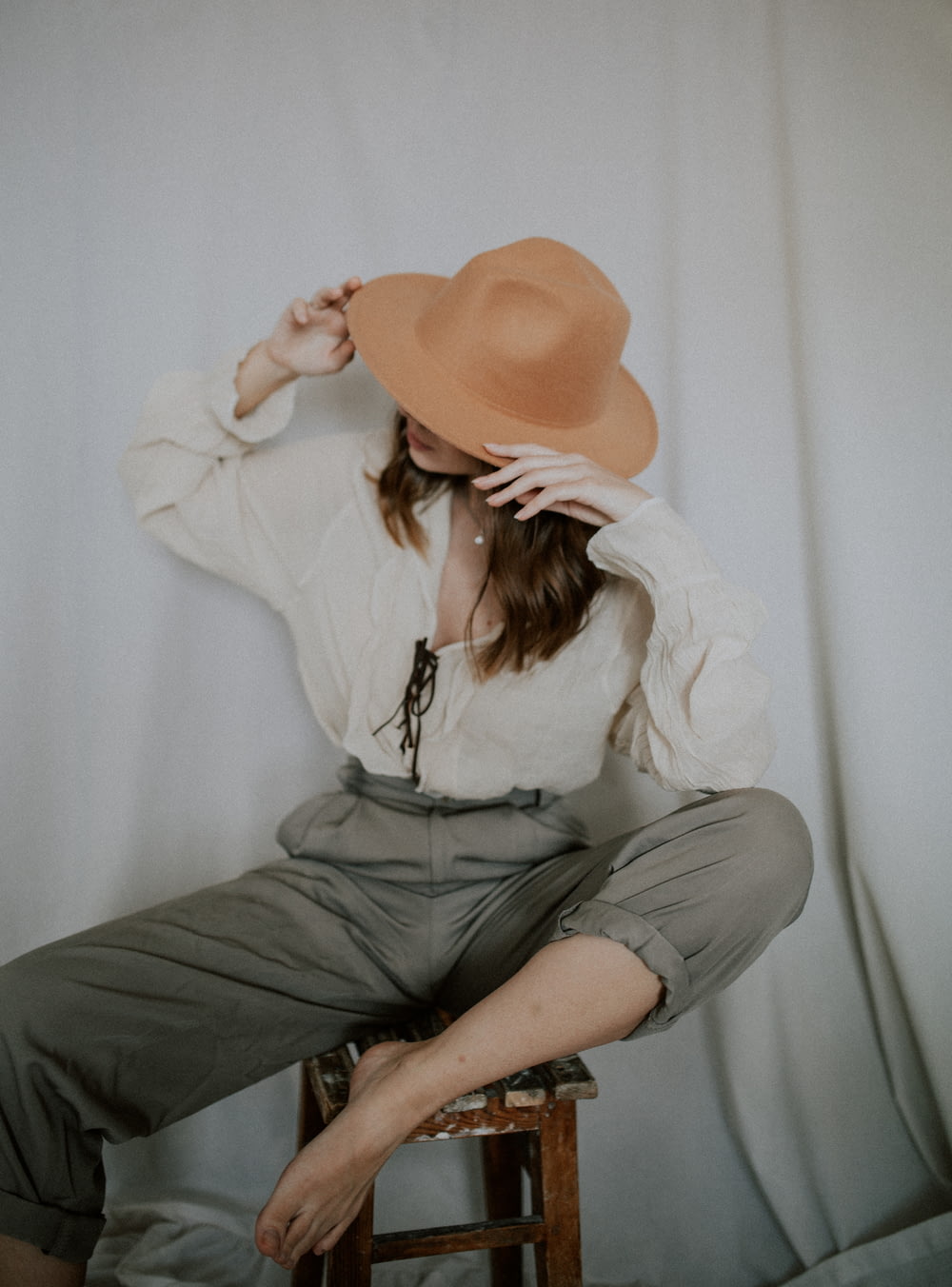 woman in white long sleeve shirt and gray skirt wearing brown fedora hat sitting on white