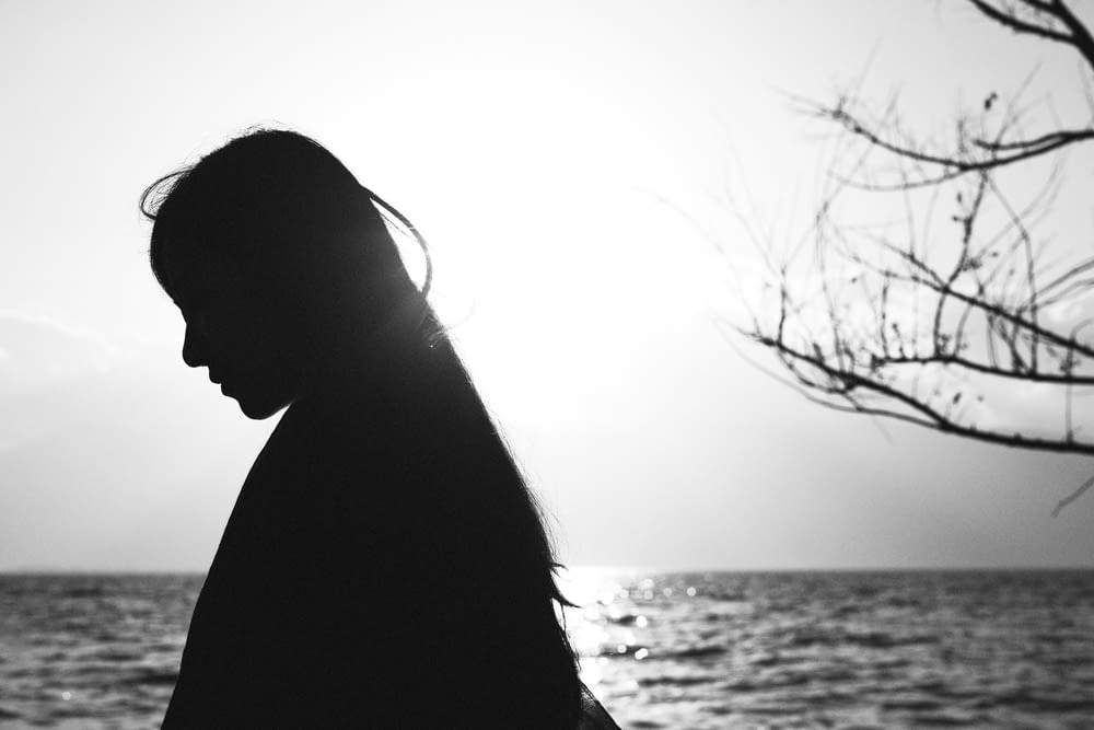silhouette of woman standing near body of water during daytime
