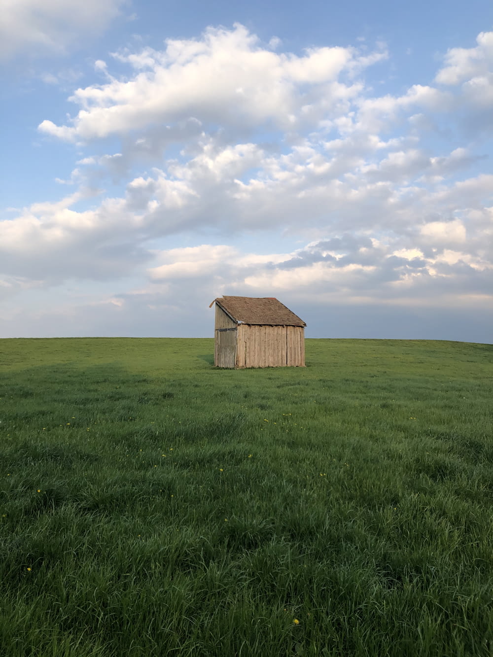 brown wooden house on green grass field under white clouds during daytime
