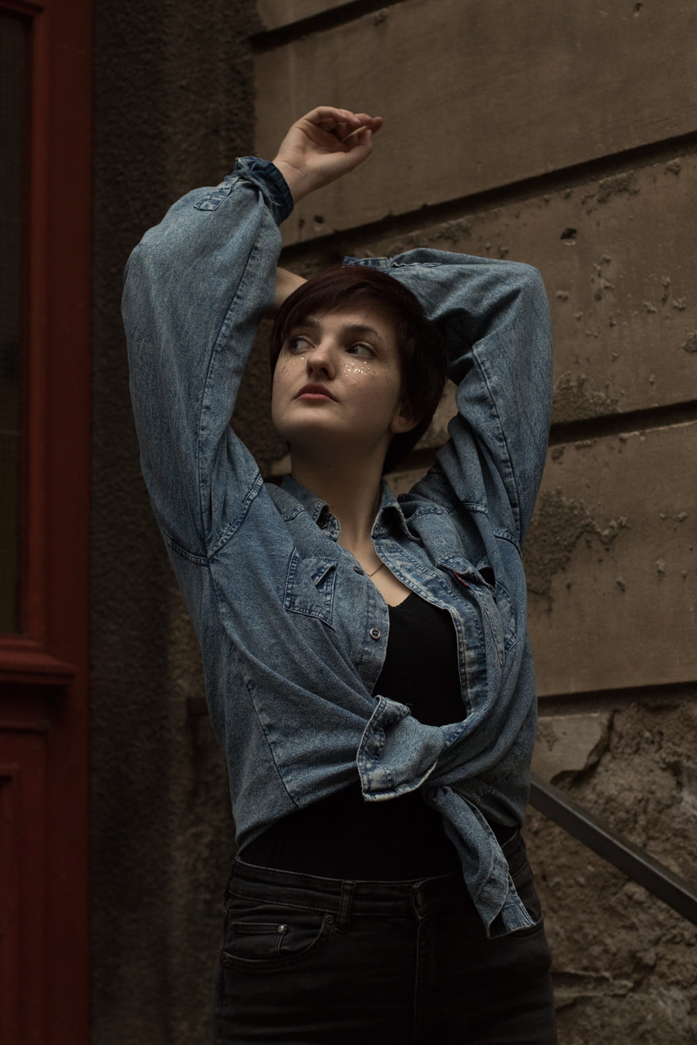 woman in blue denim jacket leaning on brown concrete wall during daytime