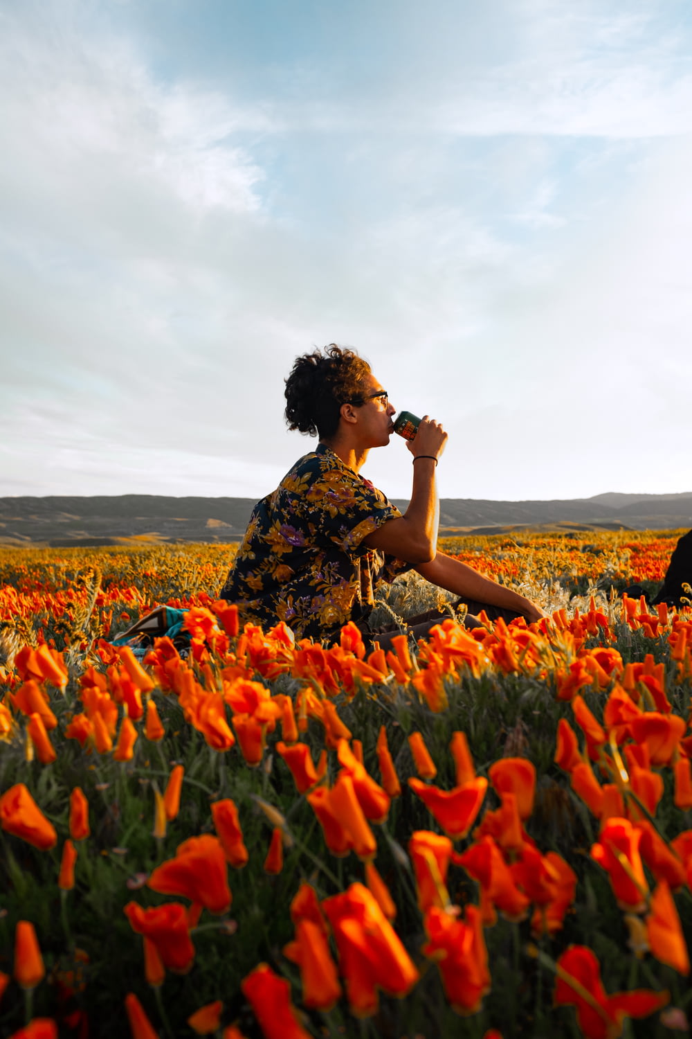 woman in black and brown floral dress sitting on red flower field during daytime