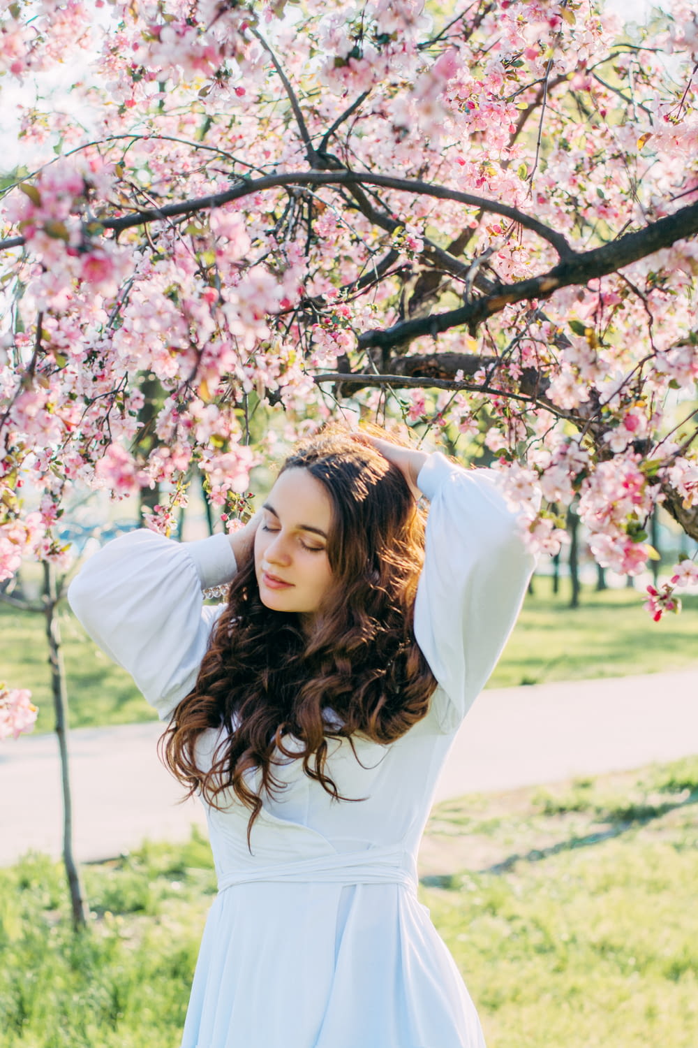 woman in white long sleeve shirt standing under pink cherry blossom tree during daytime