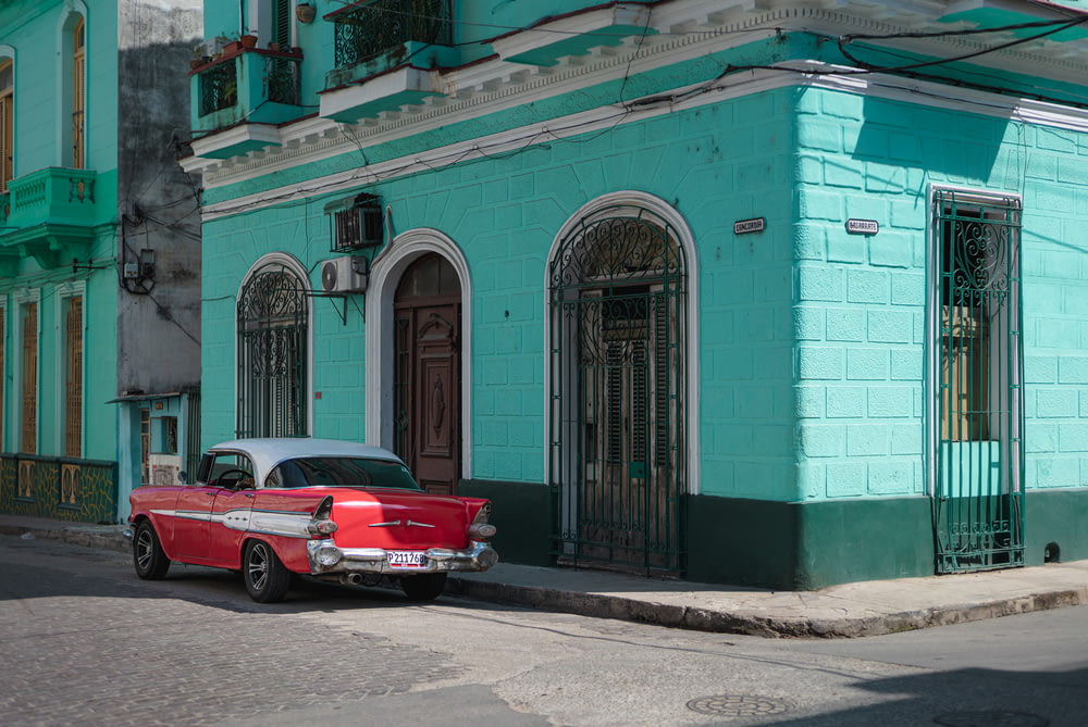 red coupe parked beside blue concrete building during daytime