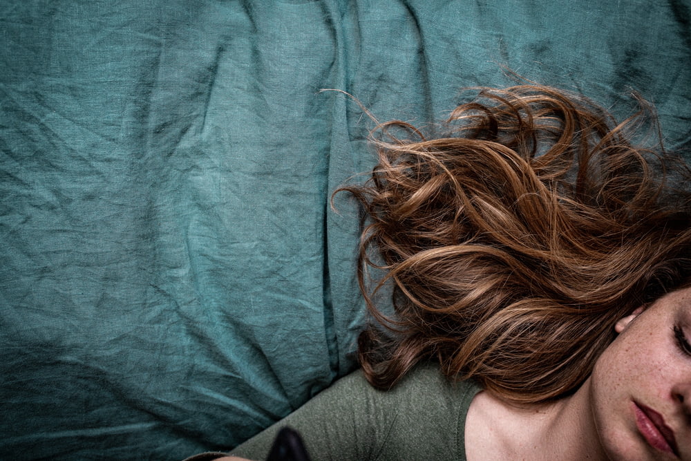 woman in gray shirt lying on blue textile