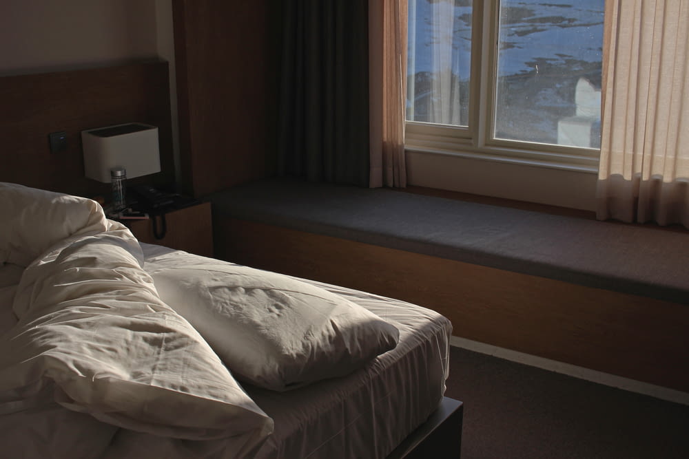 linge de lit blanc près du rideau de fenêtre marron