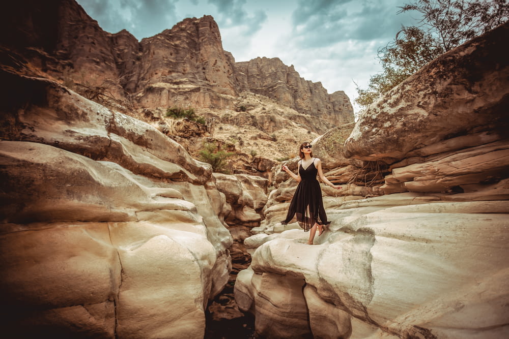 woman in black dress standing on rock formation during daytime