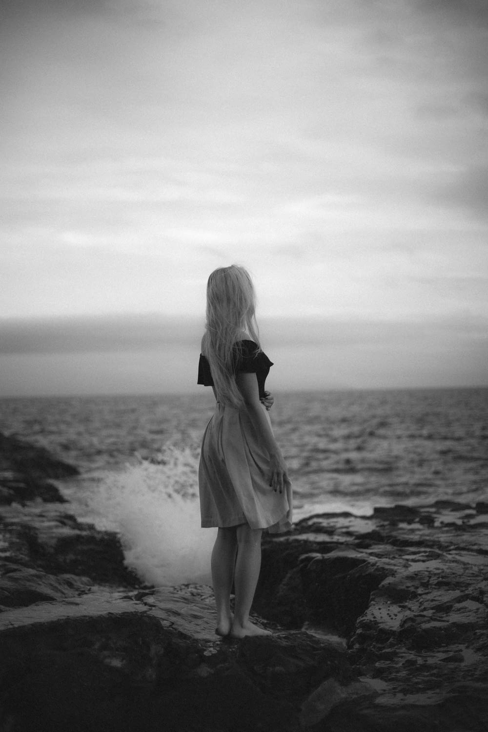 grayscale photo of woman in dress standing on beach