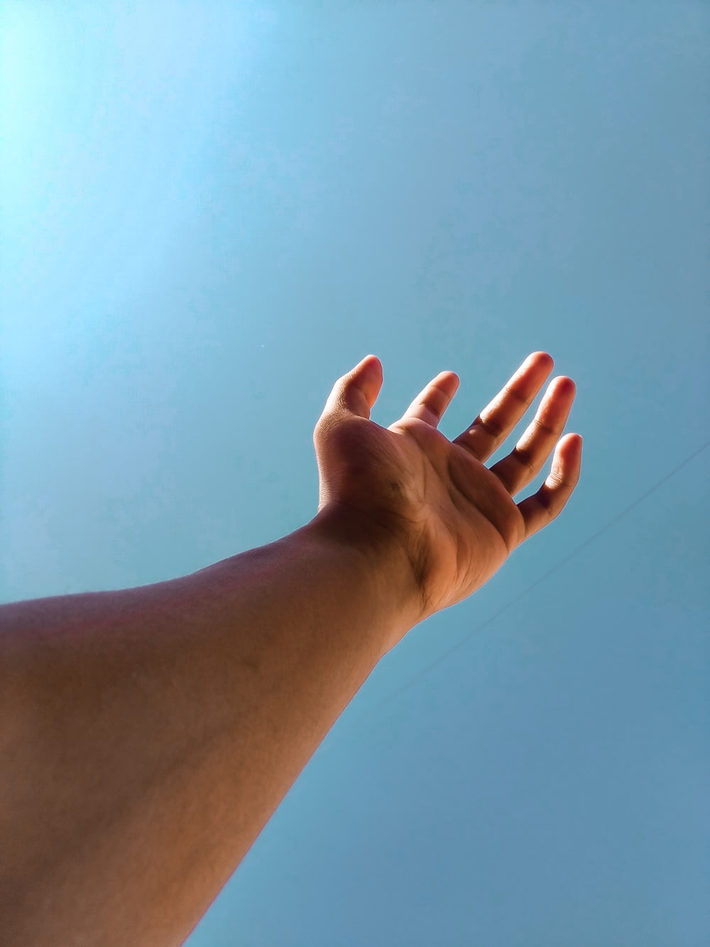 persona che alza la mano destra sotto il cielo blu durante il giorno