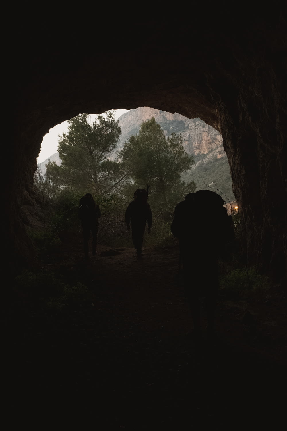 silhouette of 2 person standing inside cave during daytime