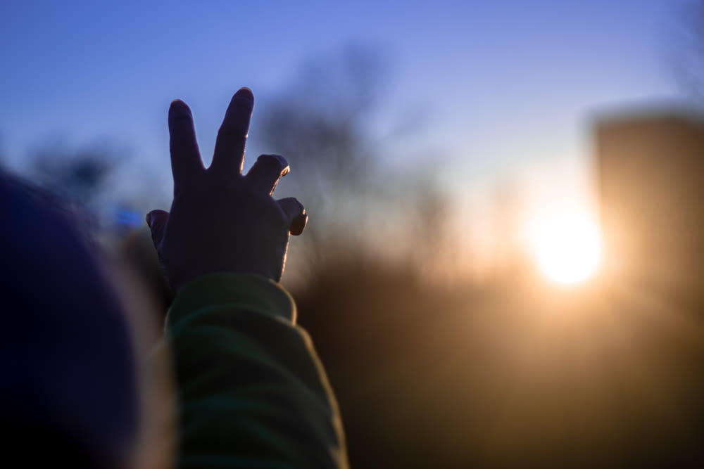 pessoa em camisa verde de manga comprida levantando a mão direita durante o pôr do sol