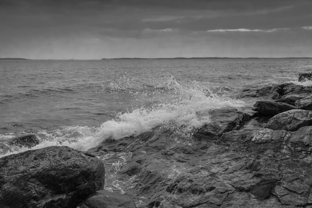 grayscale photo of ocean waves crashing on rocks