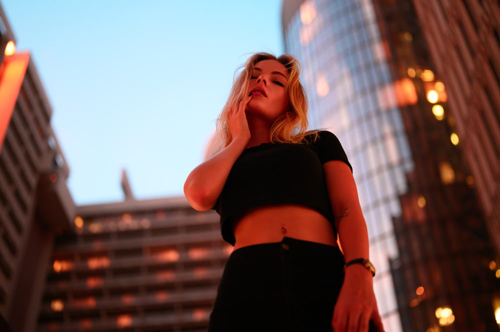 woman in black crop top and black denim bottoms standing near high rise building during daytime