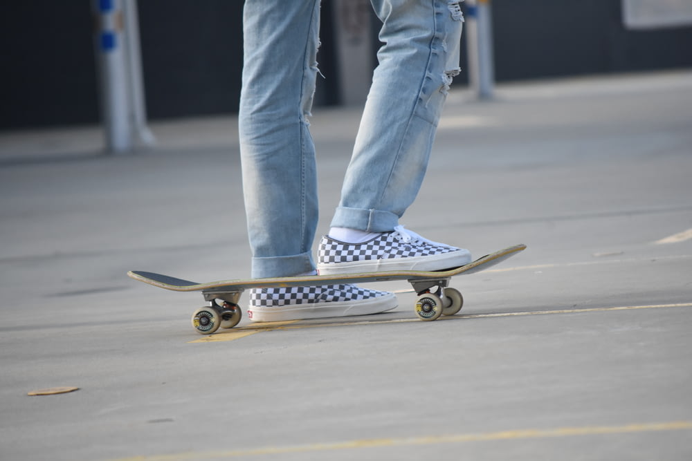 ブルーデニムのジーンズと白いスニーカーを履いた人がスケートボードに乗っている