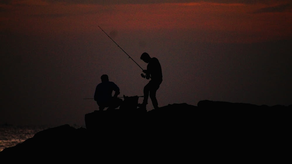 silhouette of 3 person on rock during sunset