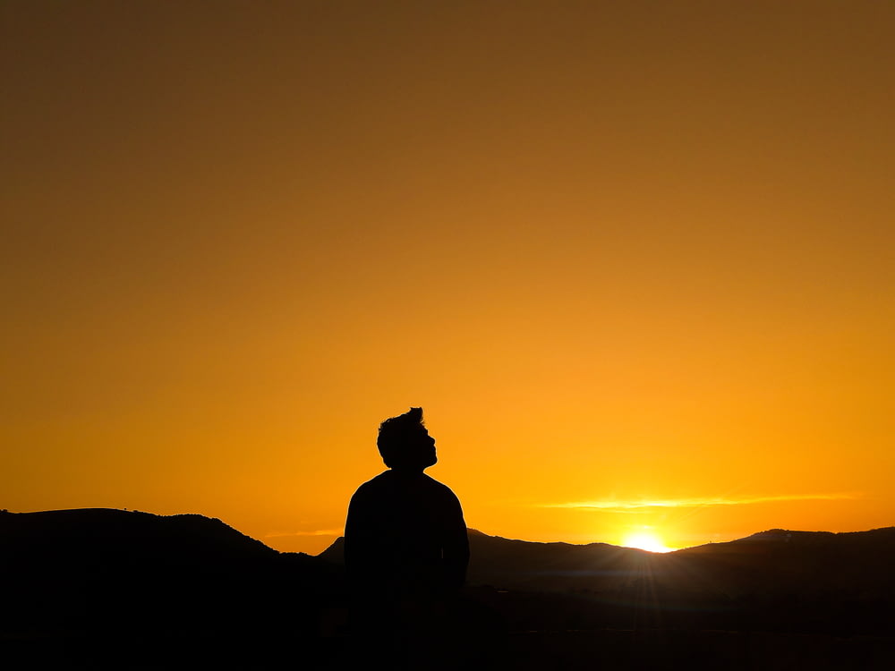 silhouette of man standing on hill during sunset