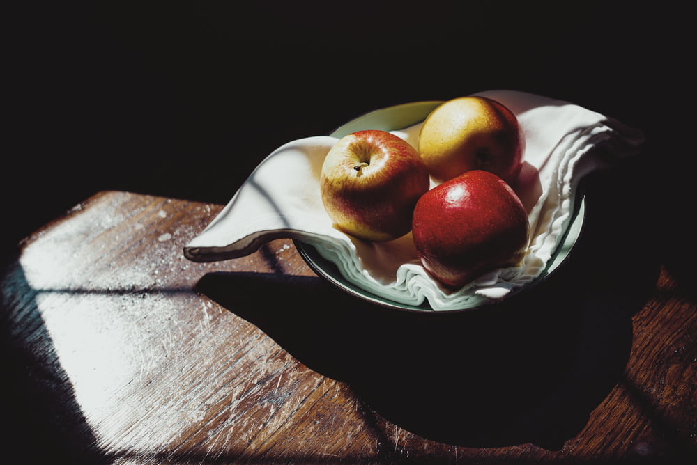 red apples on white and green floral ceramic bowl