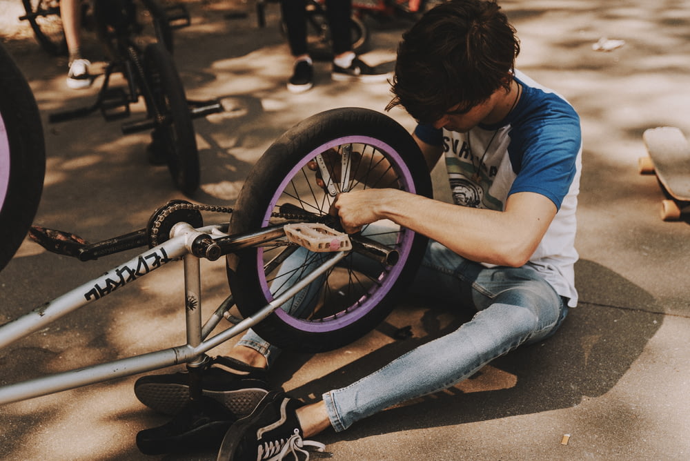 man in blue t-shirt and blue denim jeans sitting on gray concrete pavement