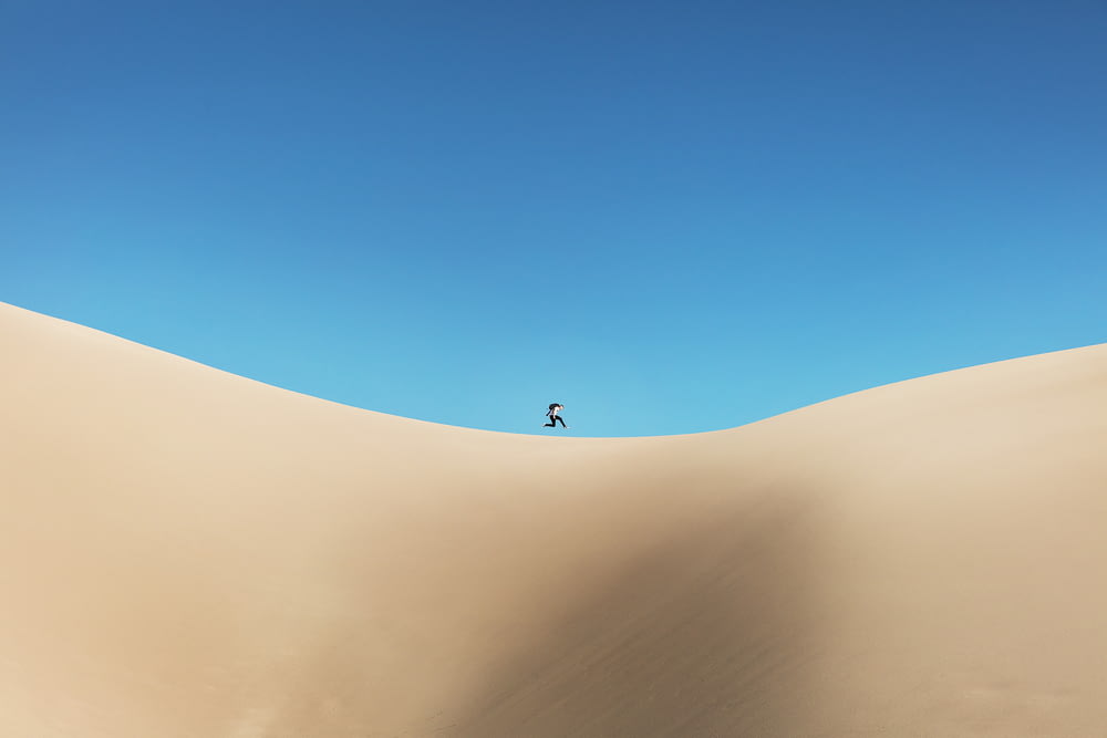 person walking on desert under blue sky during daytime