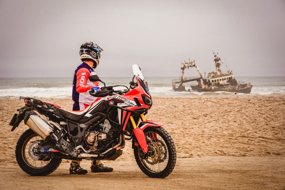 man in black and red motorcycle suit riding black and red sports bike on brown sand