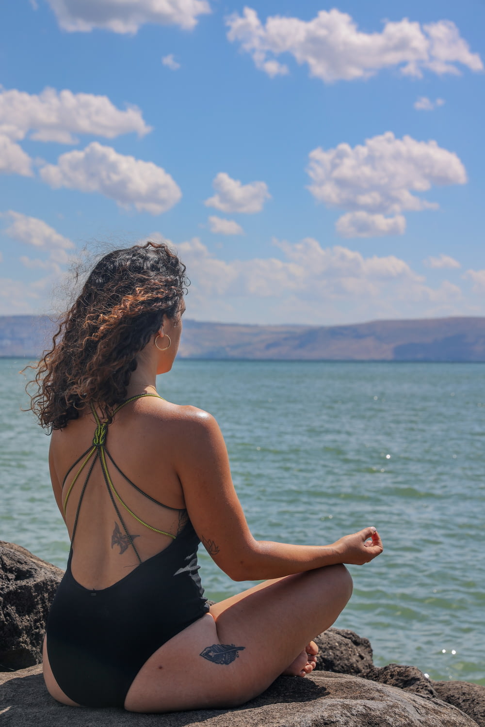 donna in bikini nero che si siede sulla roccia vicino al mare durante il giorno