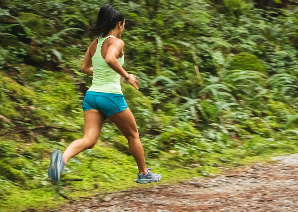 Mujer en camiseta blanca sin mangas corriendo en camino de tierra durante el día