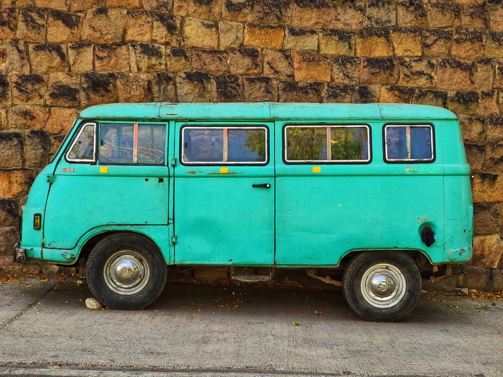 teal and white volkswagen t-2 parked beside brown brick wall