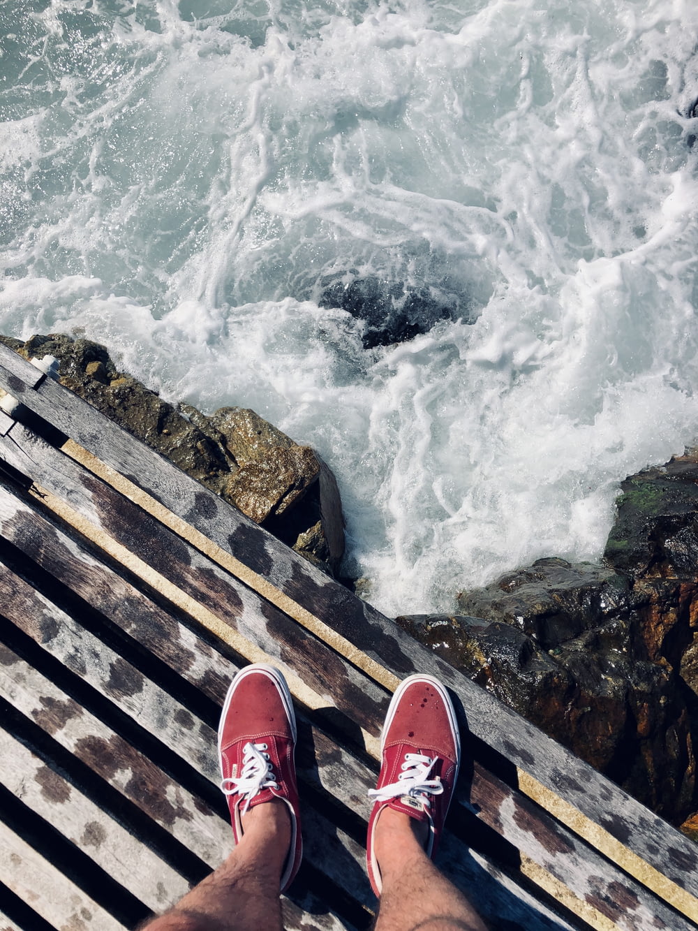 person in red and white sneakers standing on wooden dock over the water