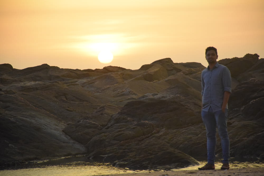 man in white long sleeve shirt standing on rock formation during sunset