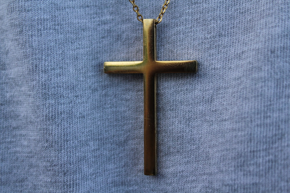 gold cross pendant necklace on blue textile
