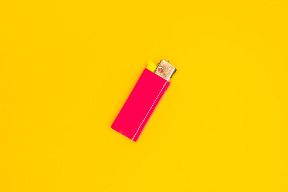 pink disposable lighter on yellow surface