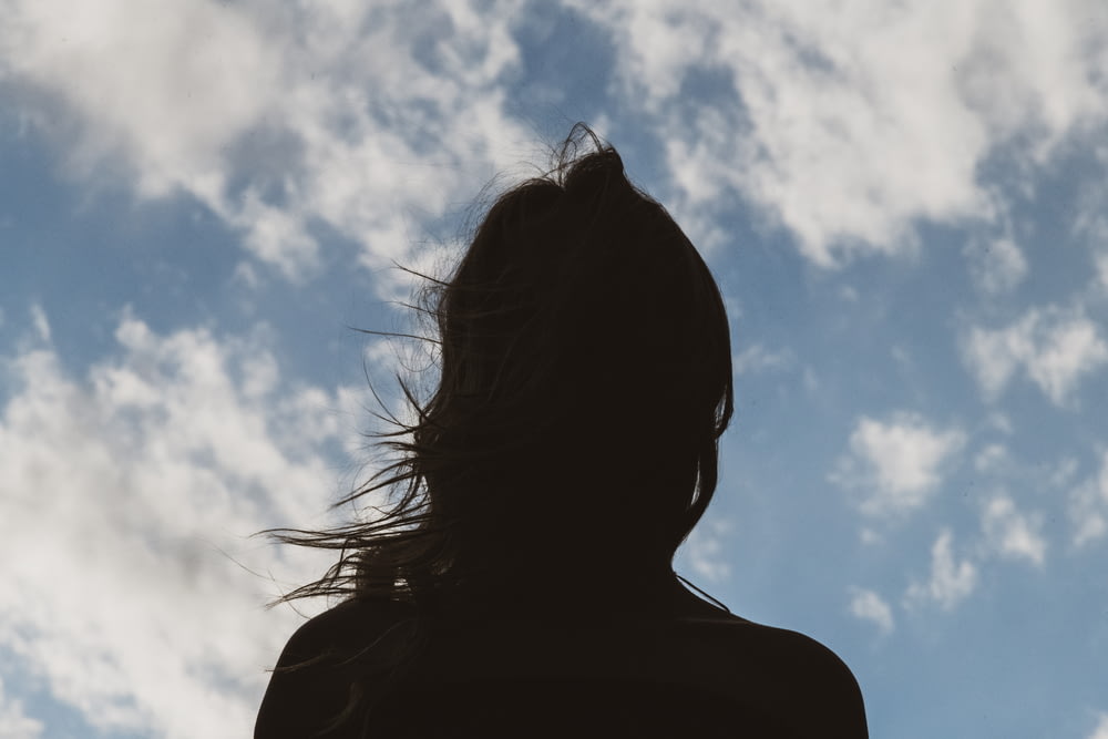 silhouette de femme sous le ciel bleu et les nuages blancs pendant la journée