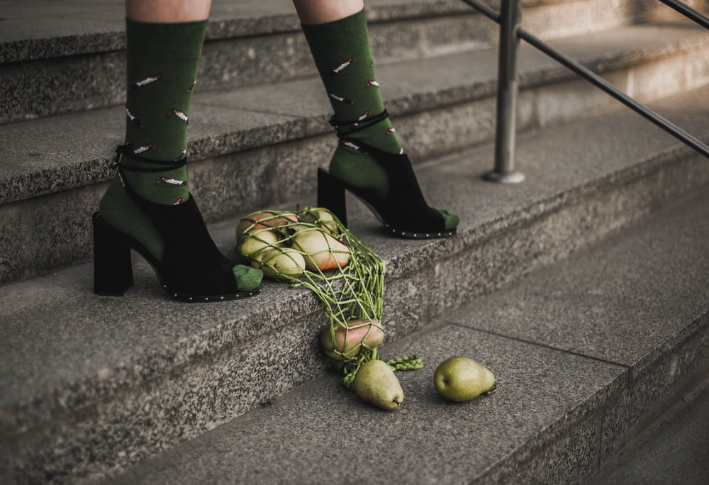 person in black rain boots holding green apple fruit