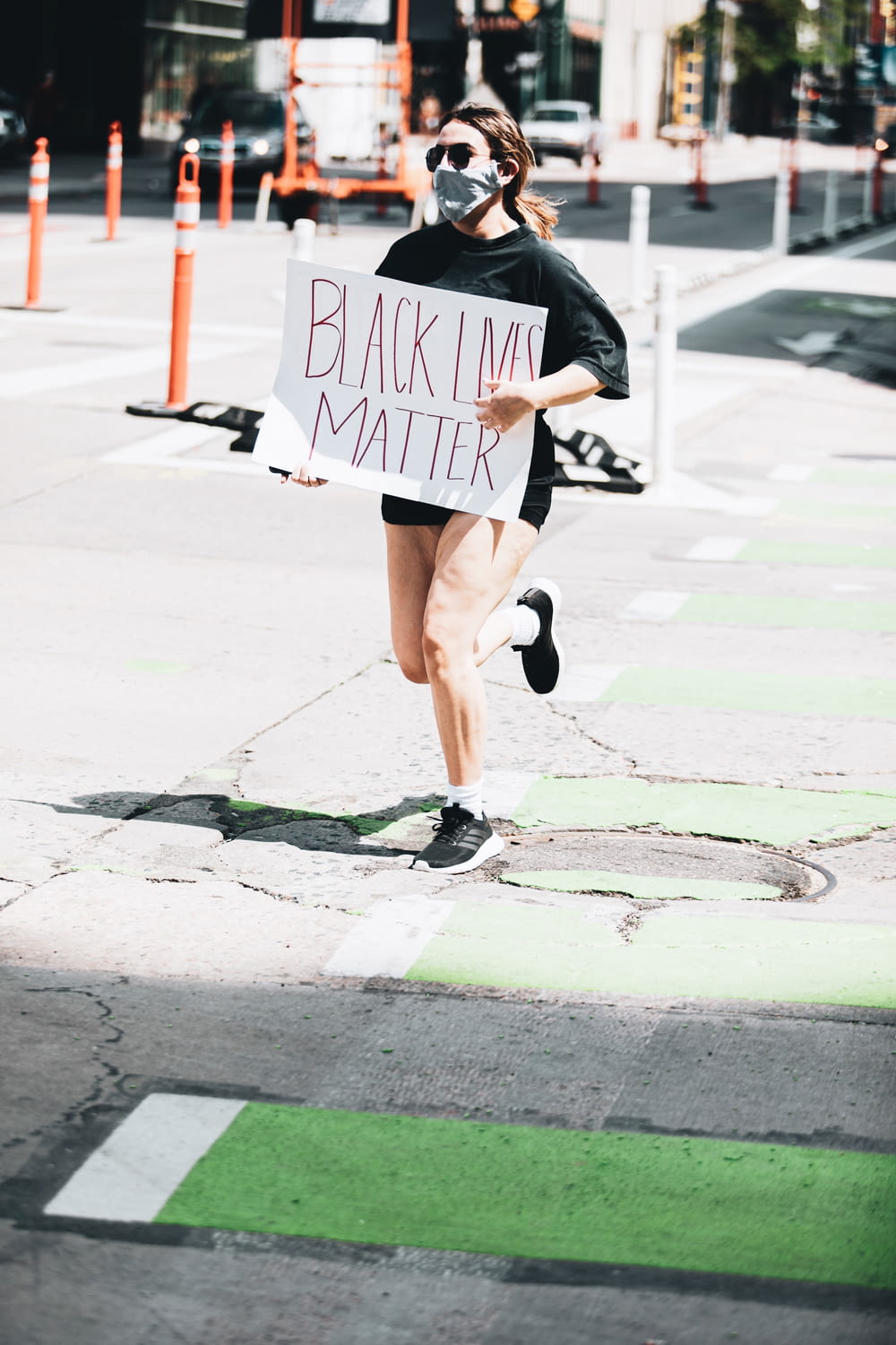 Frau in schwarzer Jacke und braunen Shorts geht tagsüber auf dem Bürgersteig spazieren