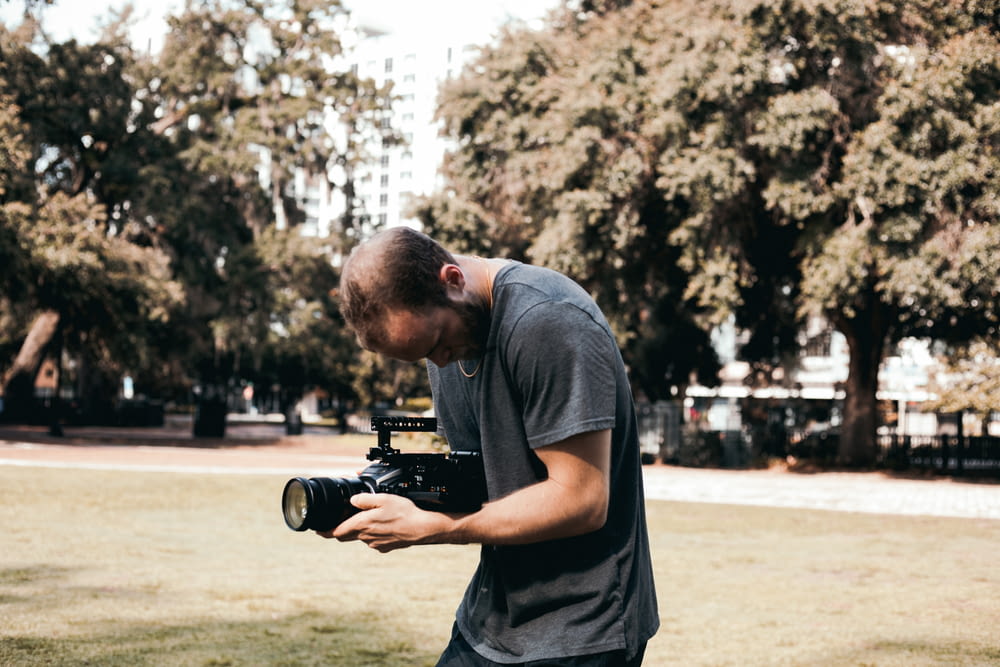man in black crew neck t-shirt holding black dslr camera during daytime