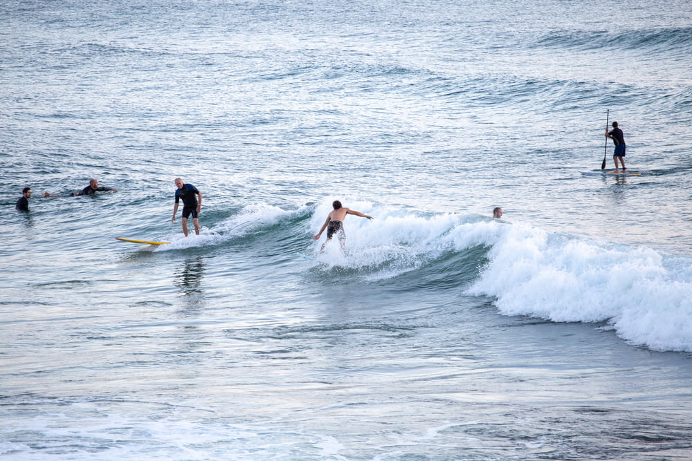 2 men surfing on sea waves during daytime