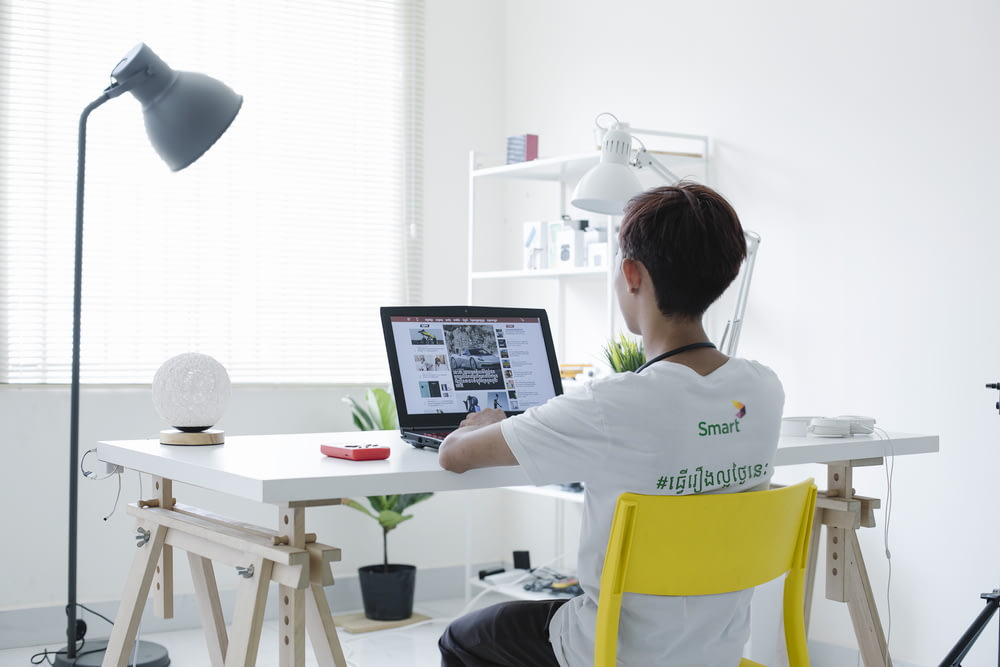 donna in camicia bianca che si siede sulla sedia usando il computer portatile