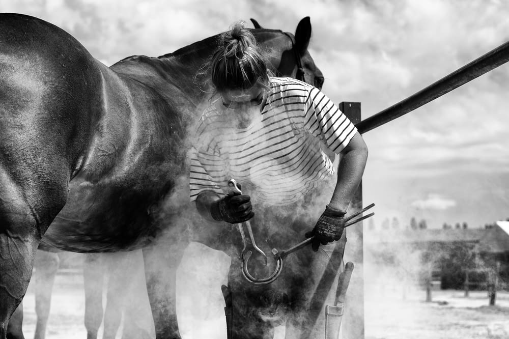 grayscale photo of woman in striped shirt riding horse