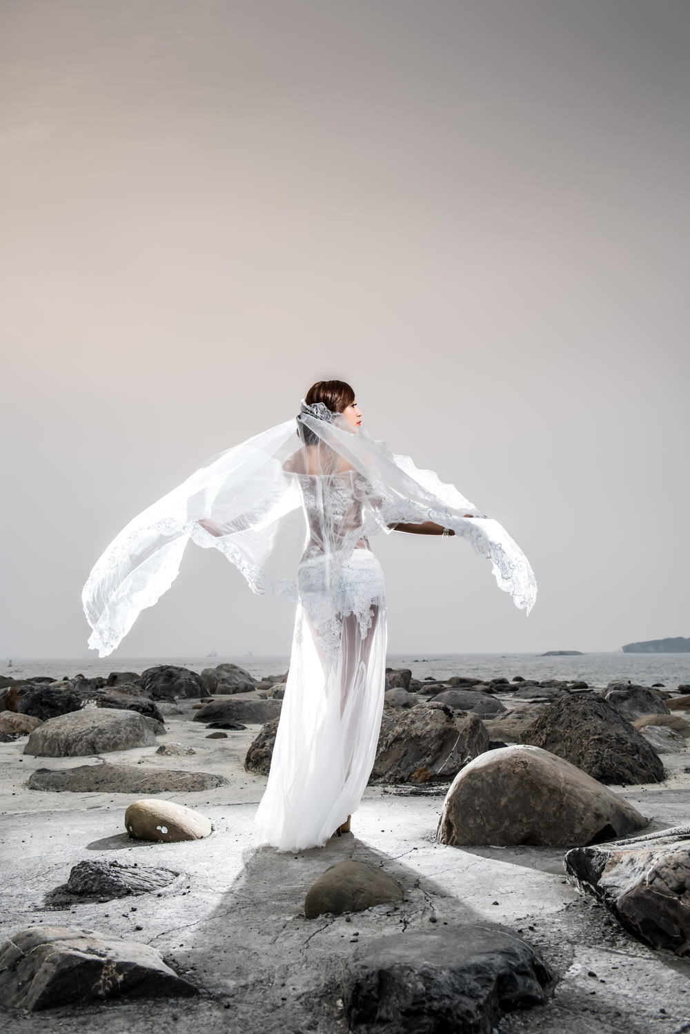 woman in white long sleeve dress standing on rocky shore during daytime