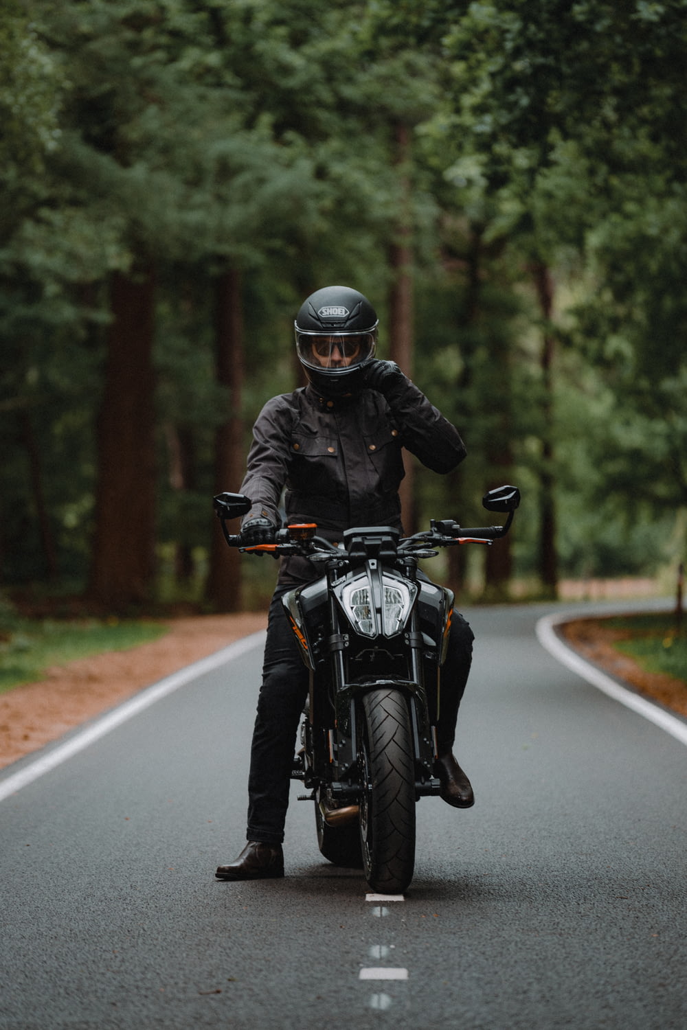 homem na jaqueta preta que monta a motocicleta na estrada durante o dia
