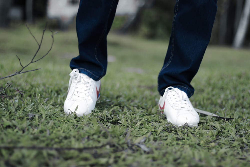 파란색 데님 청바지와 흰색 나이키 운동화를 신고 낮 동안 푸른 잔디밭에 서 있는 사람