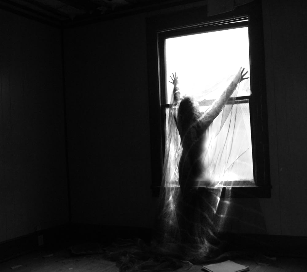 Una mujer parada frente a una ventana en una habitación oscura