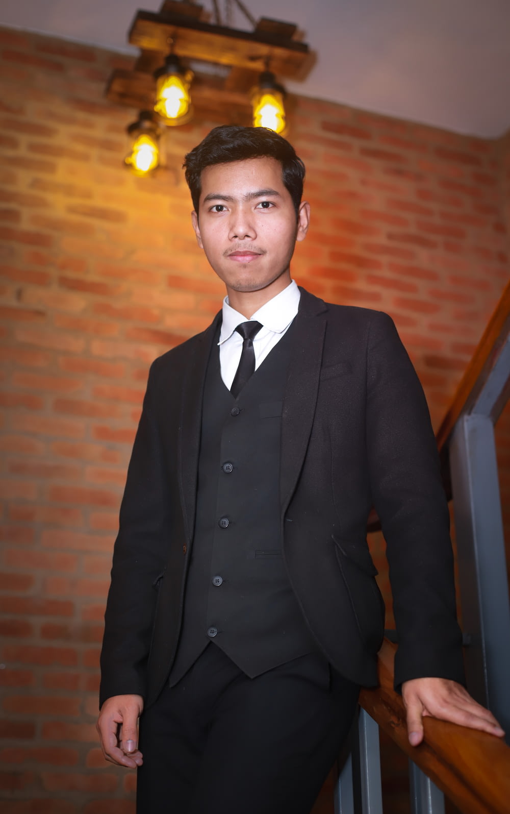man in black suit standing near brown brick wall