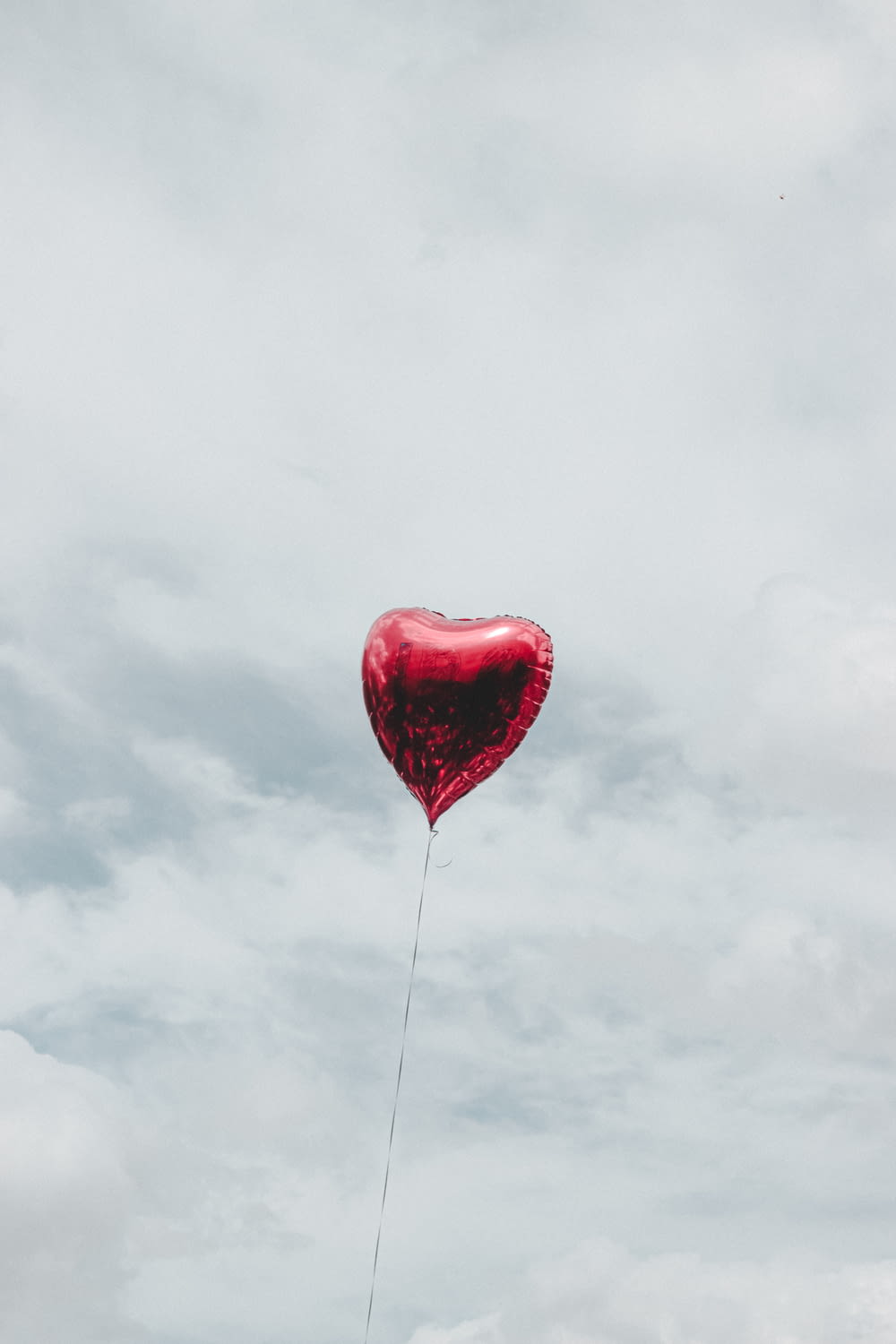 Roter Herzballon unter bewölktem Himmel